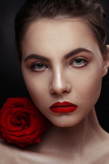 Fototapeta na wymiar Beauty fashion portrait of an elegant sexy girl with a red rose on her shoulder on a black background.