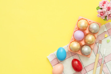 Flat lay top view colorful easter egg painted in pastel colors composition and spring flowers with paint brush on yellow pastel color background. Easter day background top view with copy space.
