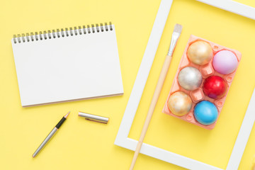 Flat lay top view colorful easter egg painted in pastel colors composition and mock up blank notebook with paint brush on yellow pastel color background. Easter day background top view with copy space
