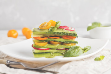 Raw vegan zucchini lasagna with vegetables and pesto sauce, light background. Vegetarian raw diet concept.