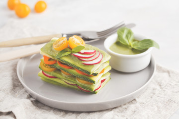 Raw vegan zucchini lasagna with vegetables and pesto sauce, light background. Vegetarian raw diet concept.