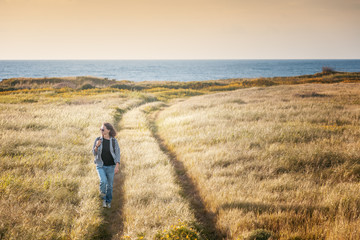 Beautiful seascape at sunset, young stylish woman traveler walks on lawn overlooking the sea