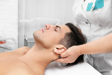 Fototapeta na wymiar Young man having neck massage in beauty salon