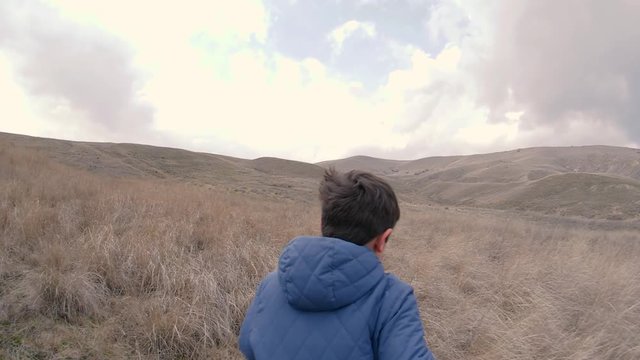 A boy on field with tall grass run to horizon with hills. Slow motion video