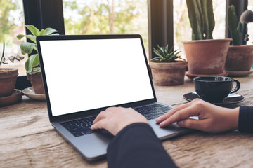 Mockup image of hands using and typing on laptop with blank white desktop screen on vintage wooden...