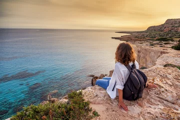 Foto op Plexiglas Cyprus Een stijlvolle jonge vrouwelijke reiziger kijkt naar een prachtige zonsondergang op de rotsen op het strand, Cyprus, Cape Greco, een populaire bestemming voor zomerreizen in Europa