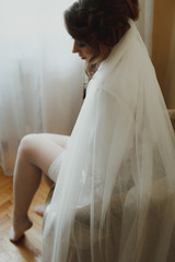 Young gorgeous bride is sitting in the room waiting for her groom. Tender light and tulle veil. Beautiful photo of bridal morning. Black and white.