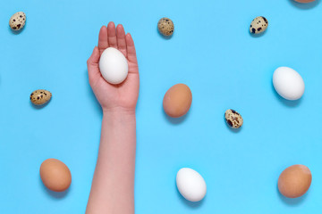 Fototapeta na wymiar Woman holding white egg in hand with eggs on blue background, copy space. Healthy food concept. Top view, flat lay. Easter eggs. Happy Easter concept