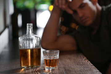 Glass and bottle of drink and blurred man on background. Alcoholism problem