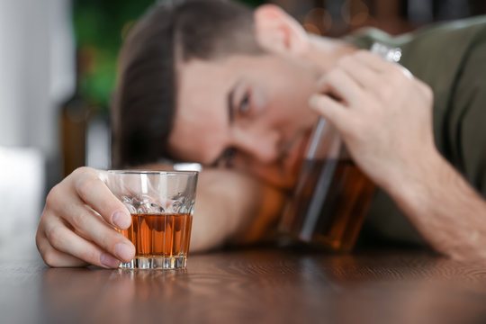 Young man with glass and bottle of drink in bar. Alcoholism problem
