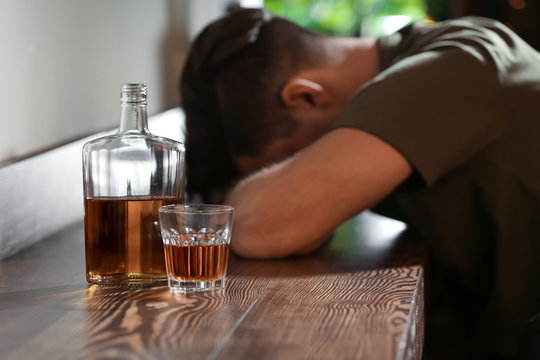 Bottle and glass with drink near unconscious drunk man in bar. Alcoholism problem