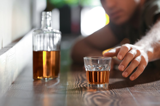 Man reaching for glass of drink in bar. Alcoholism problem
