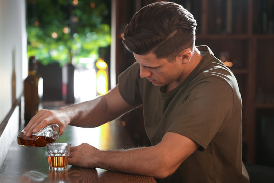 Young man pouring drink into glass at bar. Alcoholism problem