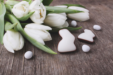 Sweets for celebrate Easter. White tulips, chocolate eggs and bunny. Old wooden background.