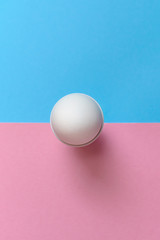 White egg standing on egg cup on blue and pink pastel background, copy space. Boiled egg in stand on paper background with two tone color. Healthy food concept. Easter egg. Flat lay, top view