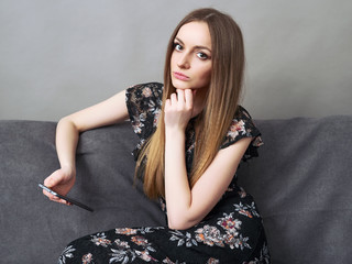Happy young adorable woman in long dress sitting on sofa with smartphone at home