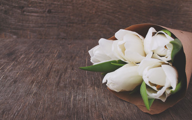 bouquet of white tulips in kraft paper on an old wooden background