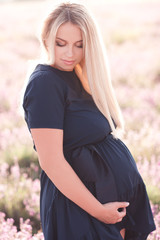 Beautiful blonde pregnant girl wearing dress outdoors. Holding tummy. Motherhood. Maternity.