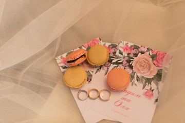 On the wedding invitation lying four pastry macaroons and wedding rings. Wedding concept.