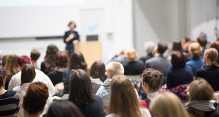 Female speaker giving presentation in lecture hall at university workshop. Audience in conference...