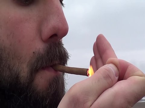 Close up view of caucasian man lighting up and smoking little cigar at dull winter day in countryside