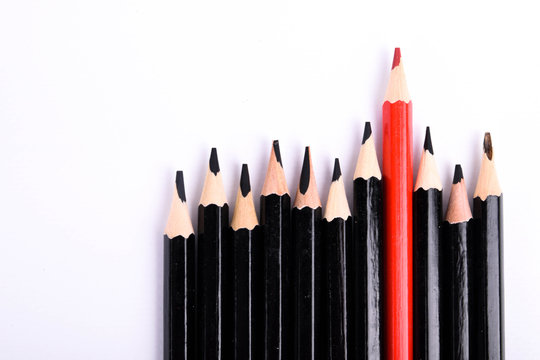 Red pencil standing out from crowd of plenty identical black fellows on white table. Leadership, uniqueness, independence,  initiative, strategy, dissent, think different, business success concept