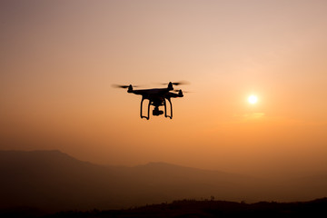Drone silhouette flying in sunset landscape. 
