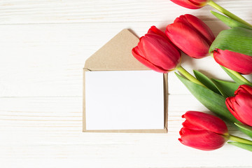 Envelope, greeting card and red tulips on white wooden background. Mock up. Flat lay with copy space.