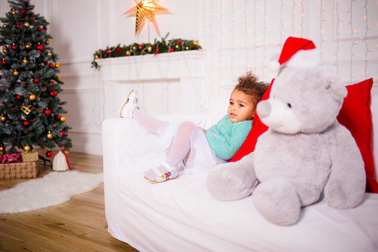 Christmas, celebration, holiday, xmas concept - happy little girl with gifts near christmas tree and fireplace