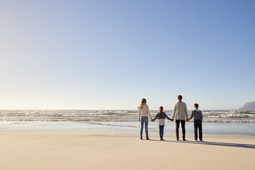 Rear View Of Family On Winter Beach Holding Hands Looking At Sea