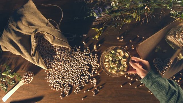 Still life with chickpeas on the table.
Slow motion. Top view. Male hands are put a saucer with chickpeas in the husks on the table.