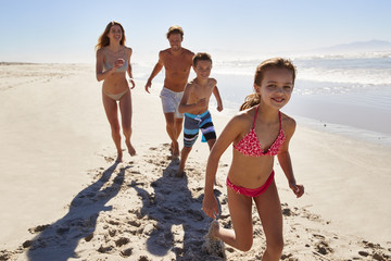 Family On Summer Vacation Running Along Beach Together