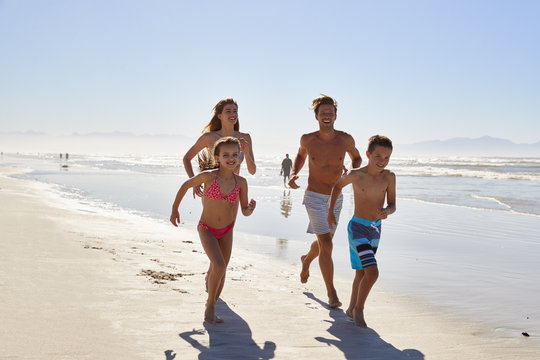 Family On Summer Vacation Running Along Beach Together