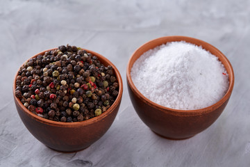 Conceptual composition of salt and pepper on spoons and bowls over light background, top view, close-up