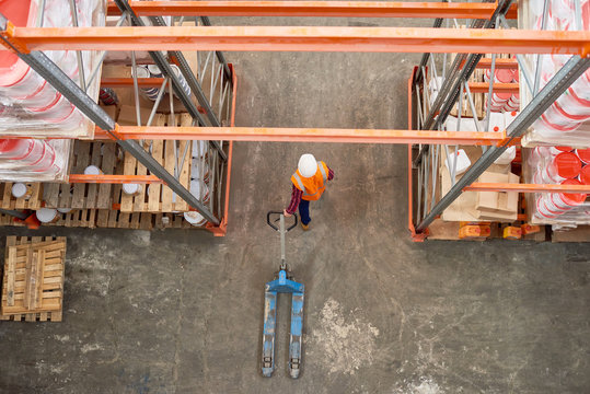 Top View Background Image Of Tall Shelf Rows In Modern Warehouse With Worker Wearing Hardhat Pulling Empty Cart In Aisle, Copy Space