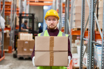 Waist up portrait of young  warehouse worker holding cardboard box and looking at camera while doing shipping and deliveries, copy space