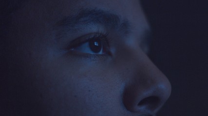 mixed race man watching tv in darkness with different color light from tv on face. Eyes closeup