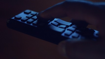 Fototapeta premium closeup of tv controller and man's hand pushing buttons in screenlight