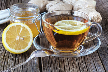 detail of cup of ginger tea with lemon and fresh ginger on wooden cutting board