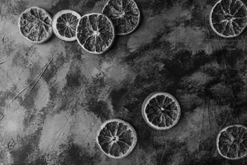 Fototapeta na wymiar Slices of dry oranges on dark stone table, black and white
