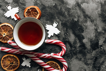 Candy canes, slices of dry oranges and cup of tea on dark stone table