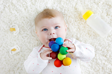 Cute baby girl playing with colorful wooden rattle toy, nursing bottle and dummy