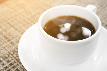 aroma hot black coffee with bokeh and smoke in white cup on the table for refreshing morning drink with space and sunlight, cup focus for bokeh on the water