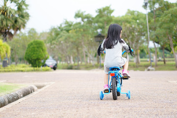Asian children cute or kid girl and black hair cycling fun on blue bike or bicycle on the public park with green garden and tree for sport exercise with healthy on summer relax holiday