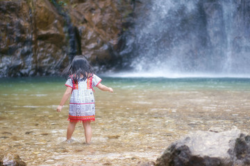 Asian children cute or turn back kid girl and hill tribe with fun and enjoy playing water splash on waterfall or river and holiday relax trip for summer at Jokkradin waterfall with space