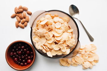 Delicious crispy cornflakes in bowl, cranberries and almonds on white background, healthy breakfast
