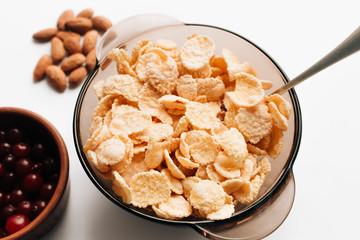 Delicious crispy cornflakes in bowl, cranberries and almonds on white background, healthy breakfast