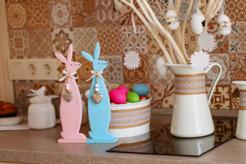 Wooden toy bunny with Easter egg on branch tree in home interior.