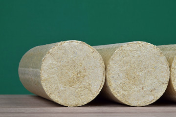Wood sawdust briquettes straightened, green background. Alternative fuel, bio fuel