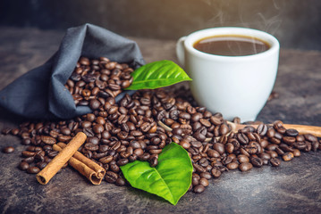 White black espresso Cup with pile of coffee beans and green leaves in bag on dark background